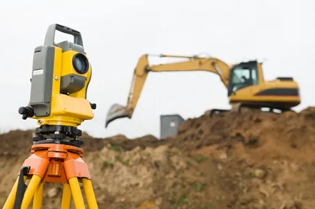 Totalstation uppställd framför grävmaskin vid anläggningsarbete